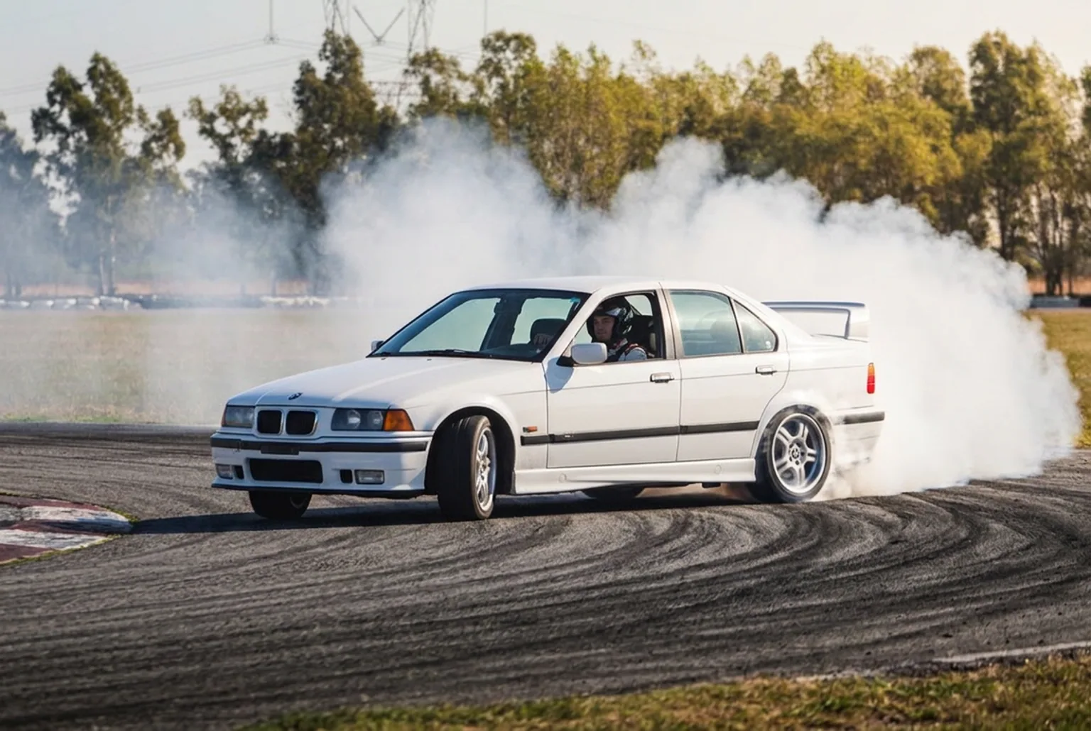 BMW E36 328i de traccion trasera derrapando con humo en las gomas durante una actividad de adrenalina para parejas