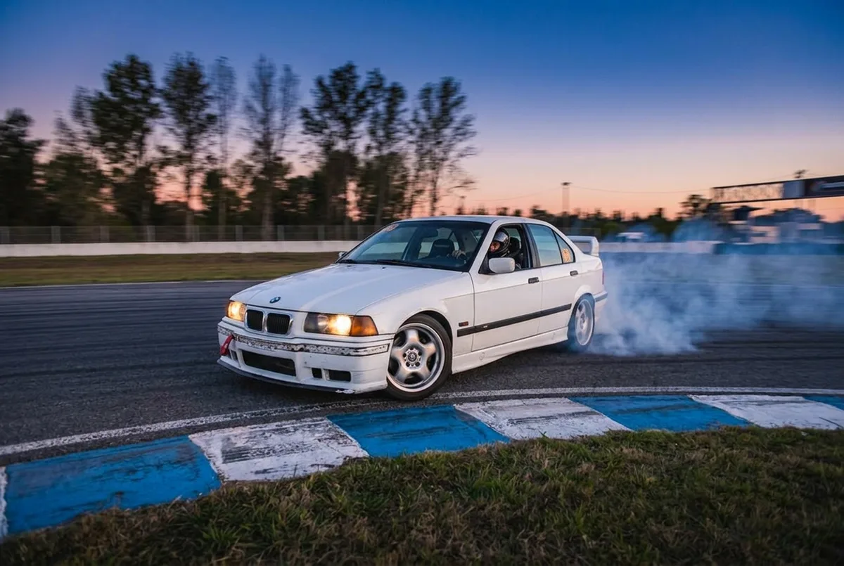 BMW E36 blanco entrando de costado en una curva tecnica de autodromo argentino al atardecer
