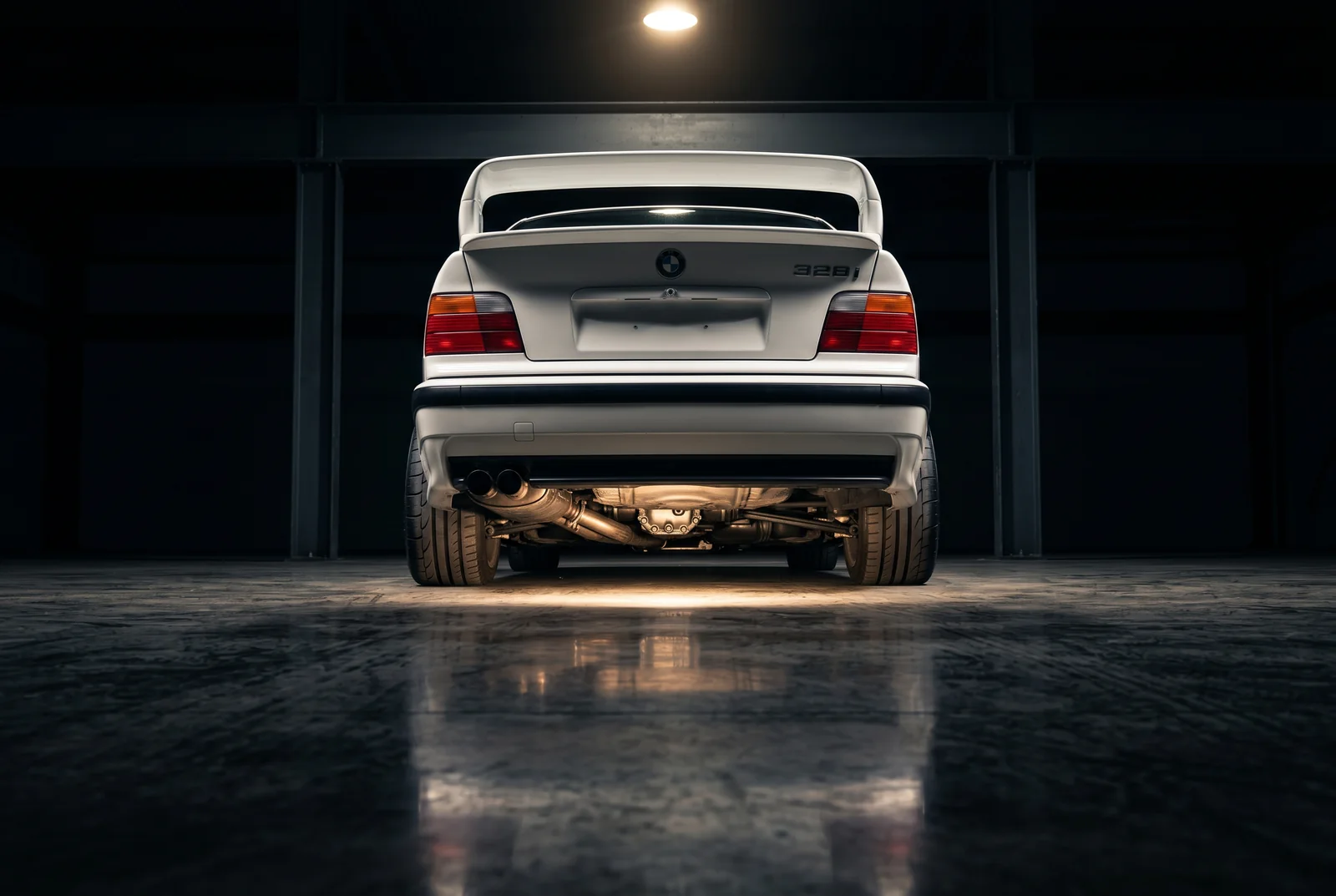 BMW E36 328i blanco con spoiler M3 GT desde angulo bajo trasero mostrando la postura del chasis y traccion trasera