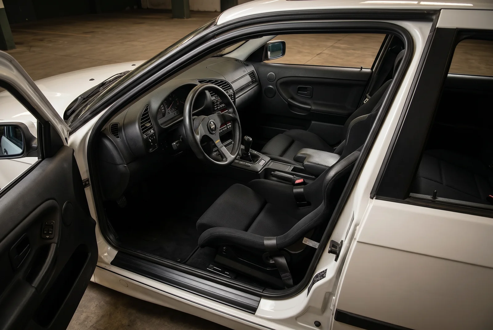 Interior stock y prolijo del BMW E36 con asientos de fabrica, cinturon de fabrica y volante deportivo, salon negro conservado
