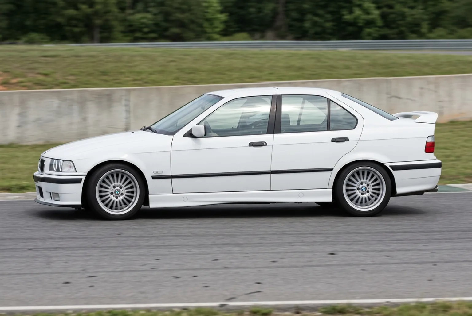 BMW E36 blanco tomando una curva del autodromo con agarre total, sin humo, en un dia de luz pareja