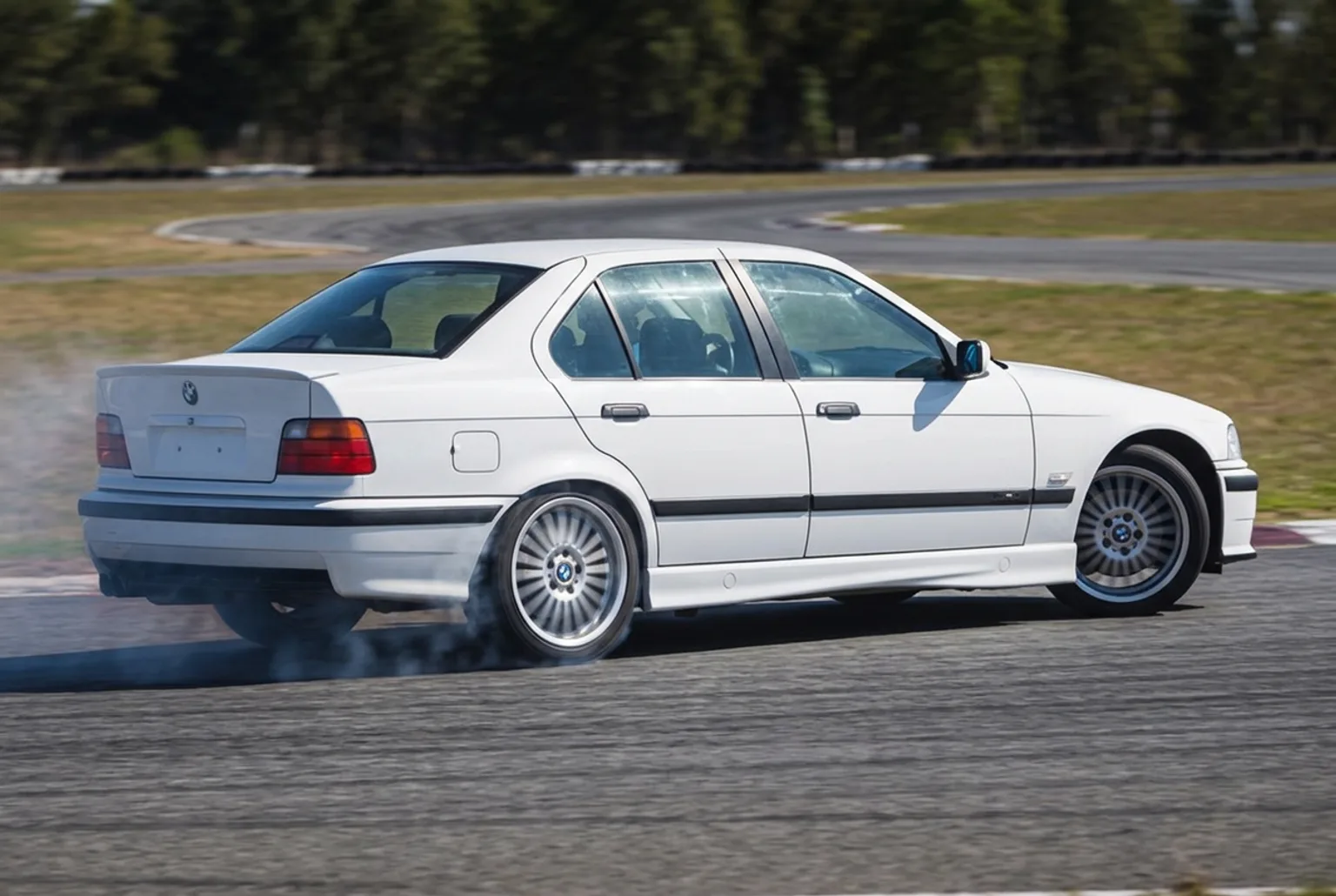 BMW E36 blanco en el instante exacto de la iniciacion del drift, con la cola saliendo y el primer humo suave en las gomas traseras