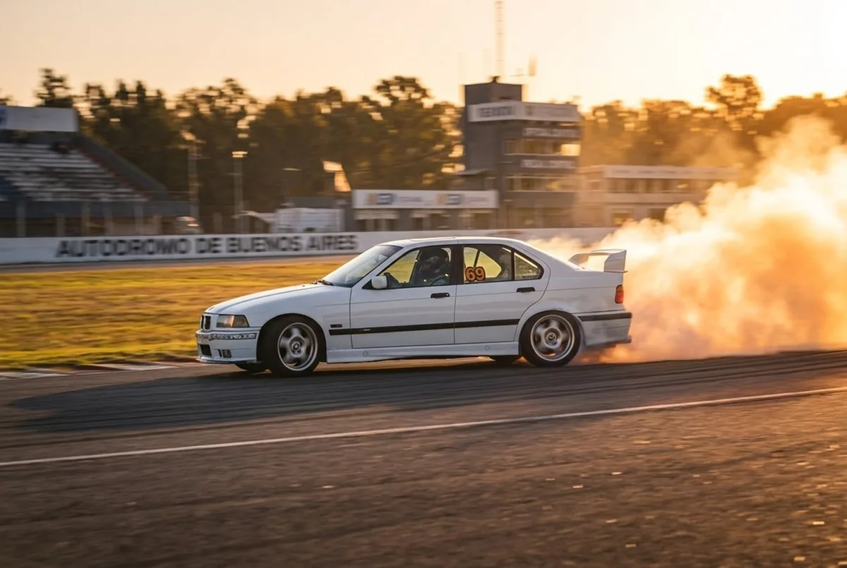 Белый BMW E36 номер 69 в широком заносе с огромным облаком дыма от покрышек в контровом свете заходящего солнца
