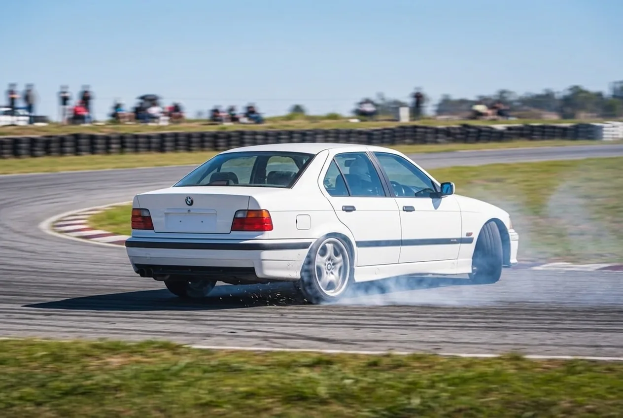 Vista trasera del BMW E36 con el tren trasero escapando de costado y humo, mostrando el sobreviraje