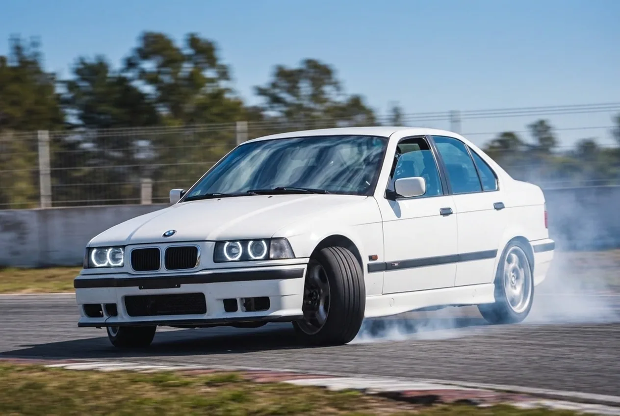 BMW E36 tomando una curva con transferencia de peso, plano bajo, goma cargada y humo