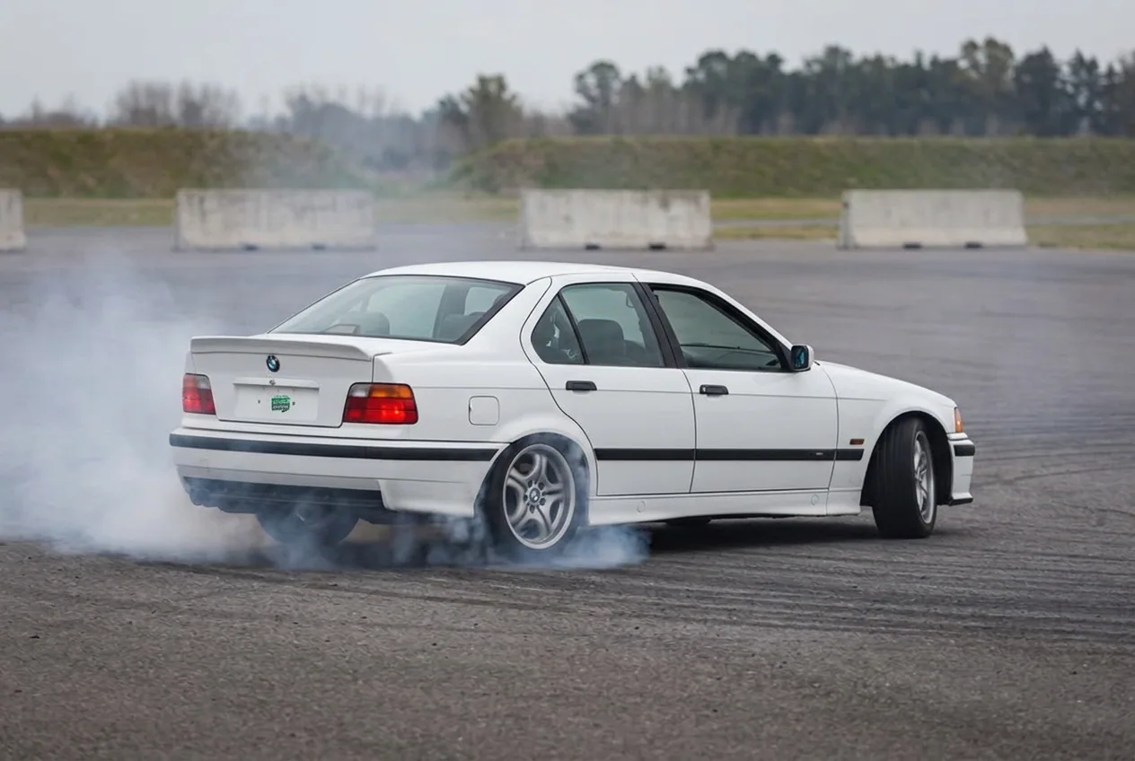 BMW E36 blanco de tracción trasera en pleno donut con las ruedas delanteras giradas y las traseras humeando