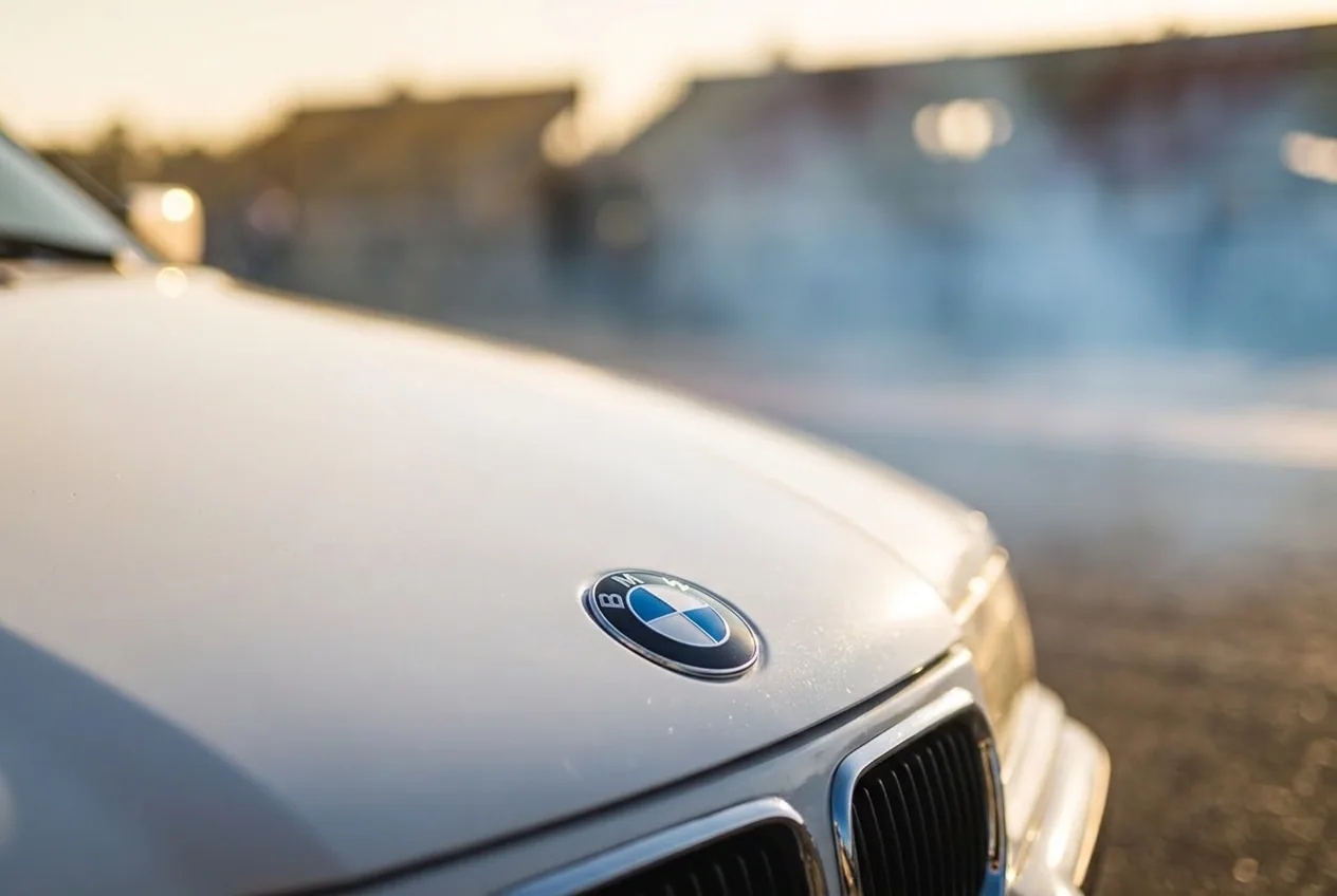 Detalle del emblema BMW en el capot blanco del E36 a la hora dorada, reserva tu clase de drift de regalo por WhatsApp