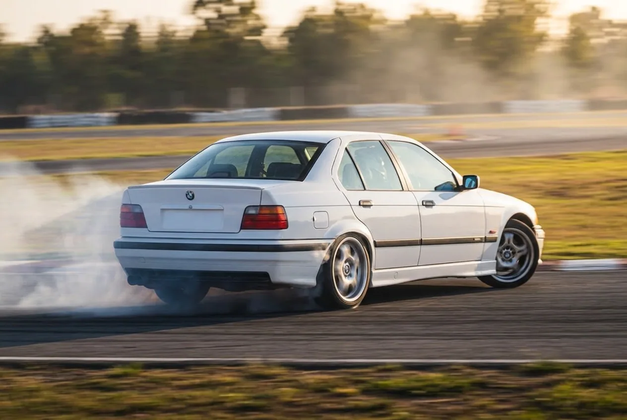 White BMW E36 switching direction between two linked corners, a drift transition with lateral smoke