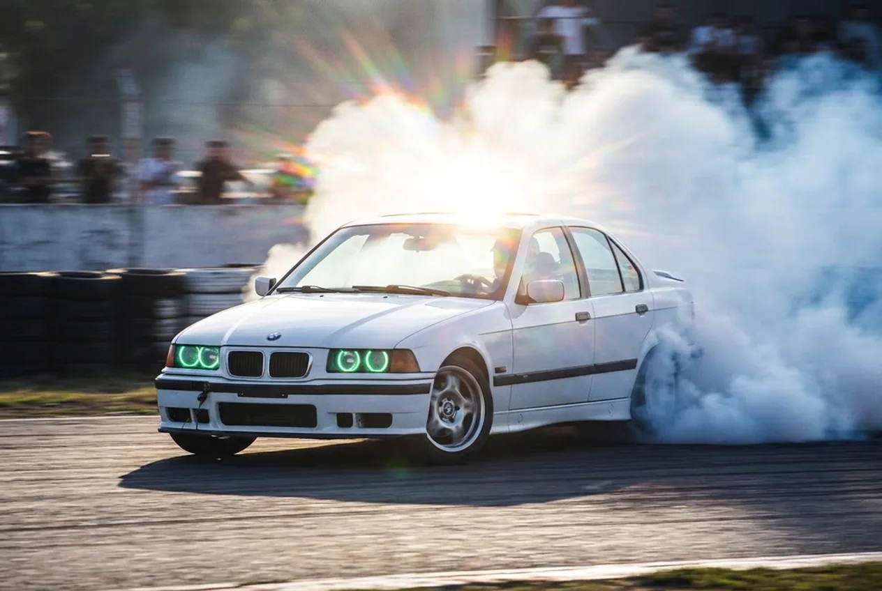 White BMW E36 at extreme angle and high speed throwing up a large cloud of smoke on track