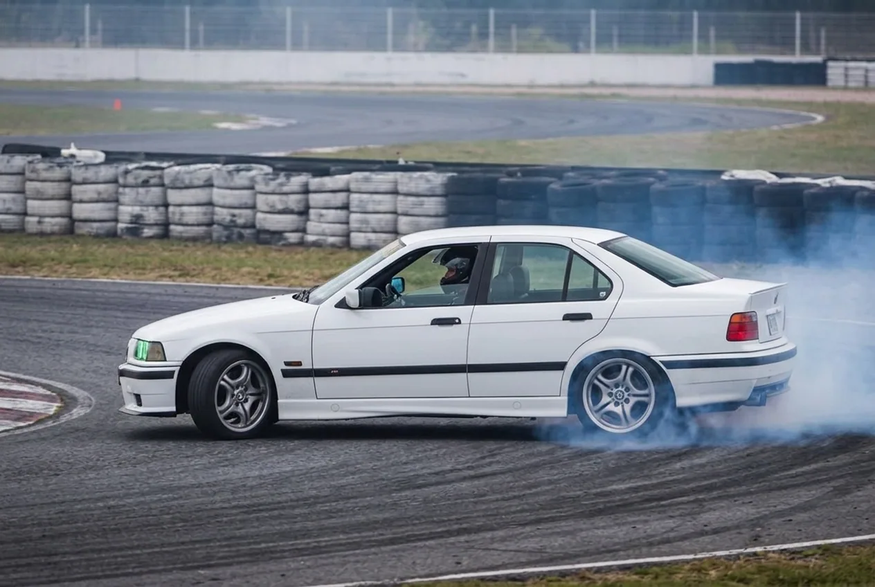 BMW E36 blanco derrapando con humo y el horizonte de Buenos Aires de fondo bajo cielo despejado