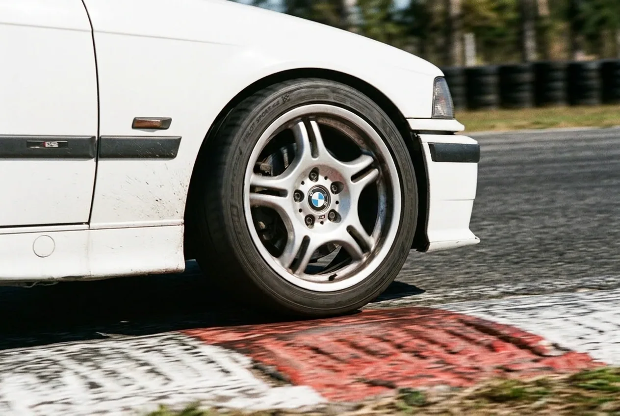 La rueda delantera del BMW E36 blanco pisando el piano rojo y blanco en la trazada de un circuito