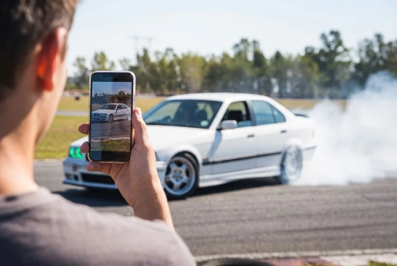 Un amigo filma con el celular mientras el BMW E36 blanco derrapa en la pista — despedida de soltero en grupo