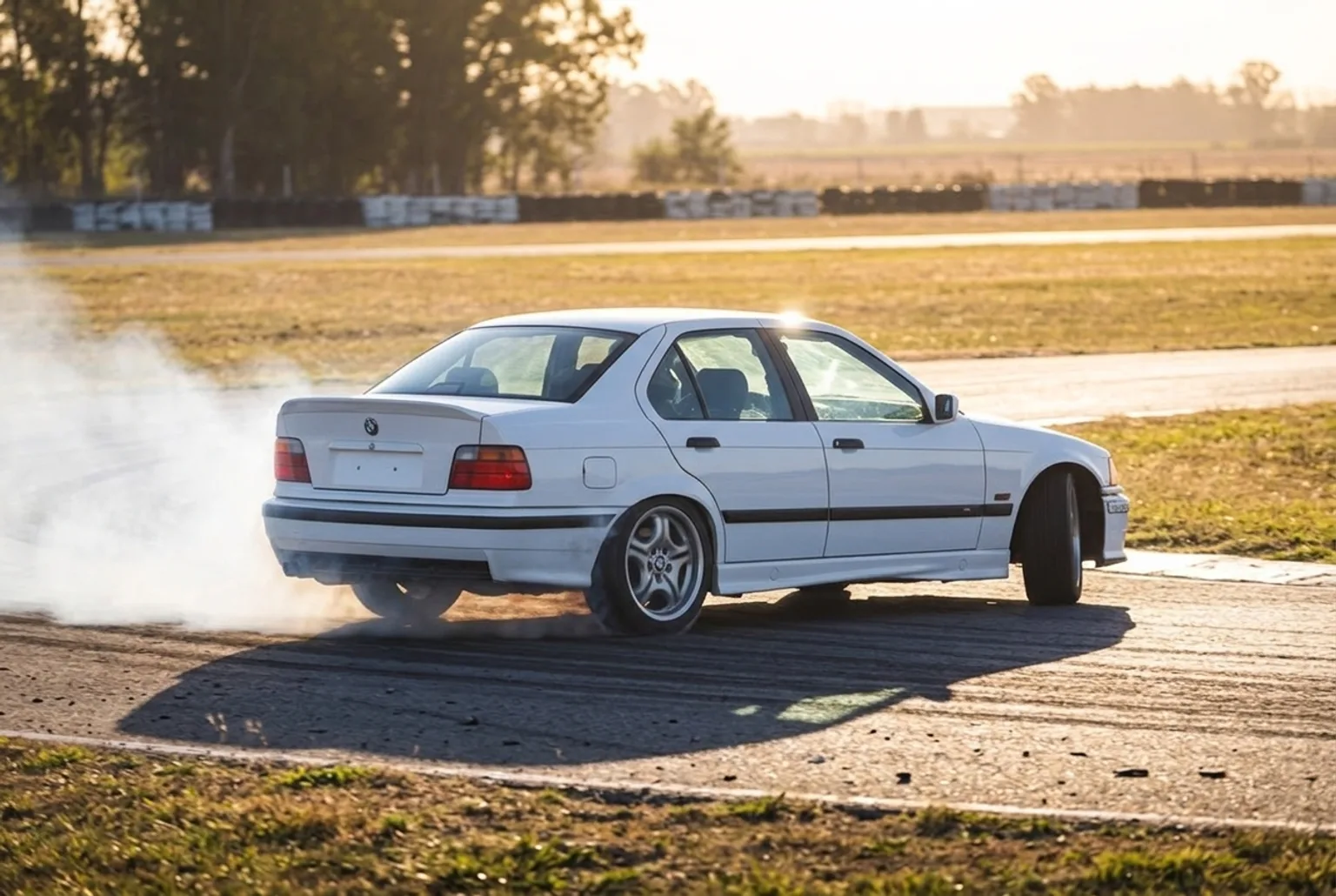 BMW E36 blanco derrapando con humo en las gomas en pista cerrada al atardecer cerca de Buenos Aires