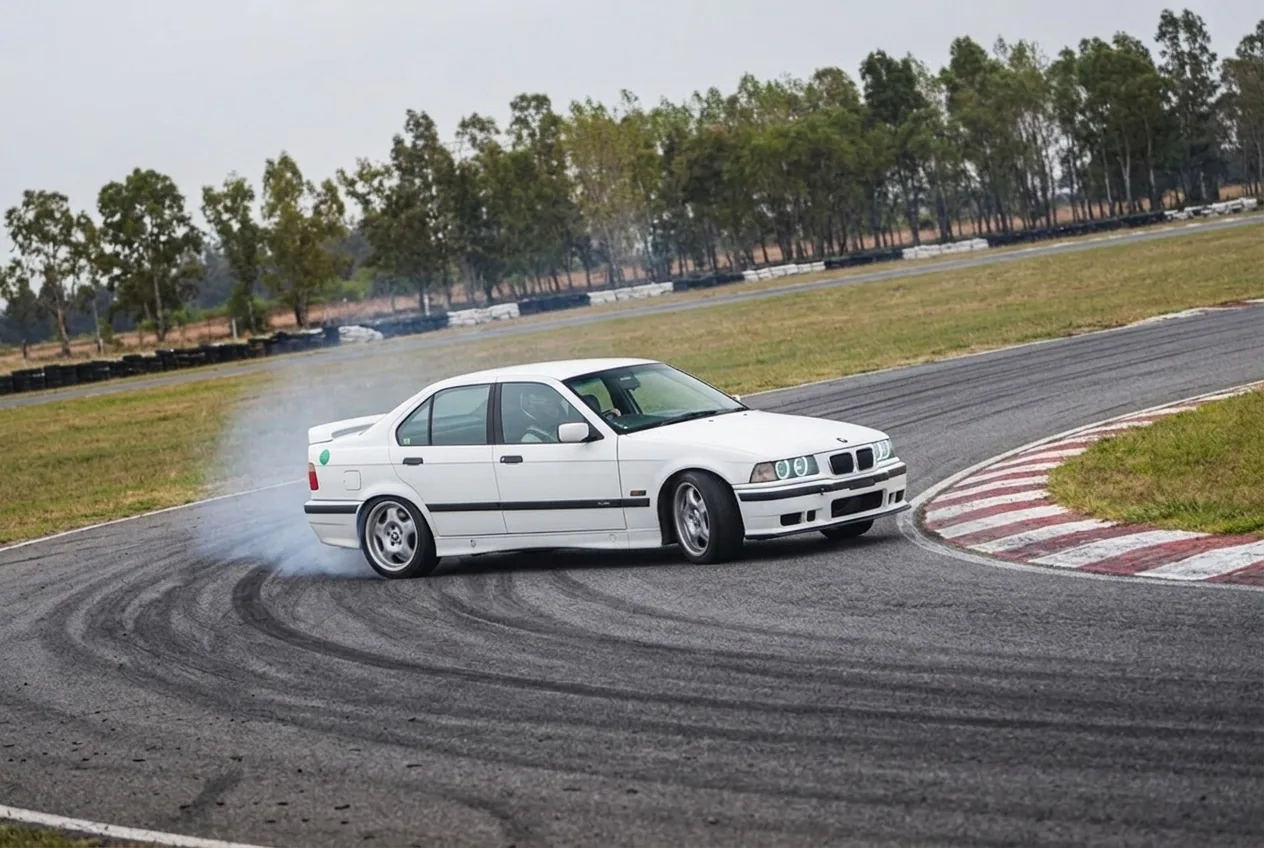 BMW E36 blanco drifteando sobre la trazada en una curva de circuito cerrado, leer la línea