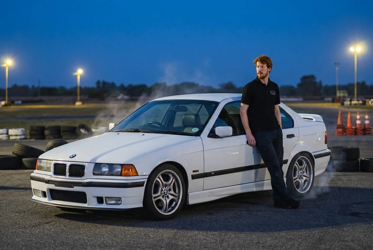 El instructor pelirrojo junto al BMW E36 blanco en el paddock tras una sesion de drift al atardecer