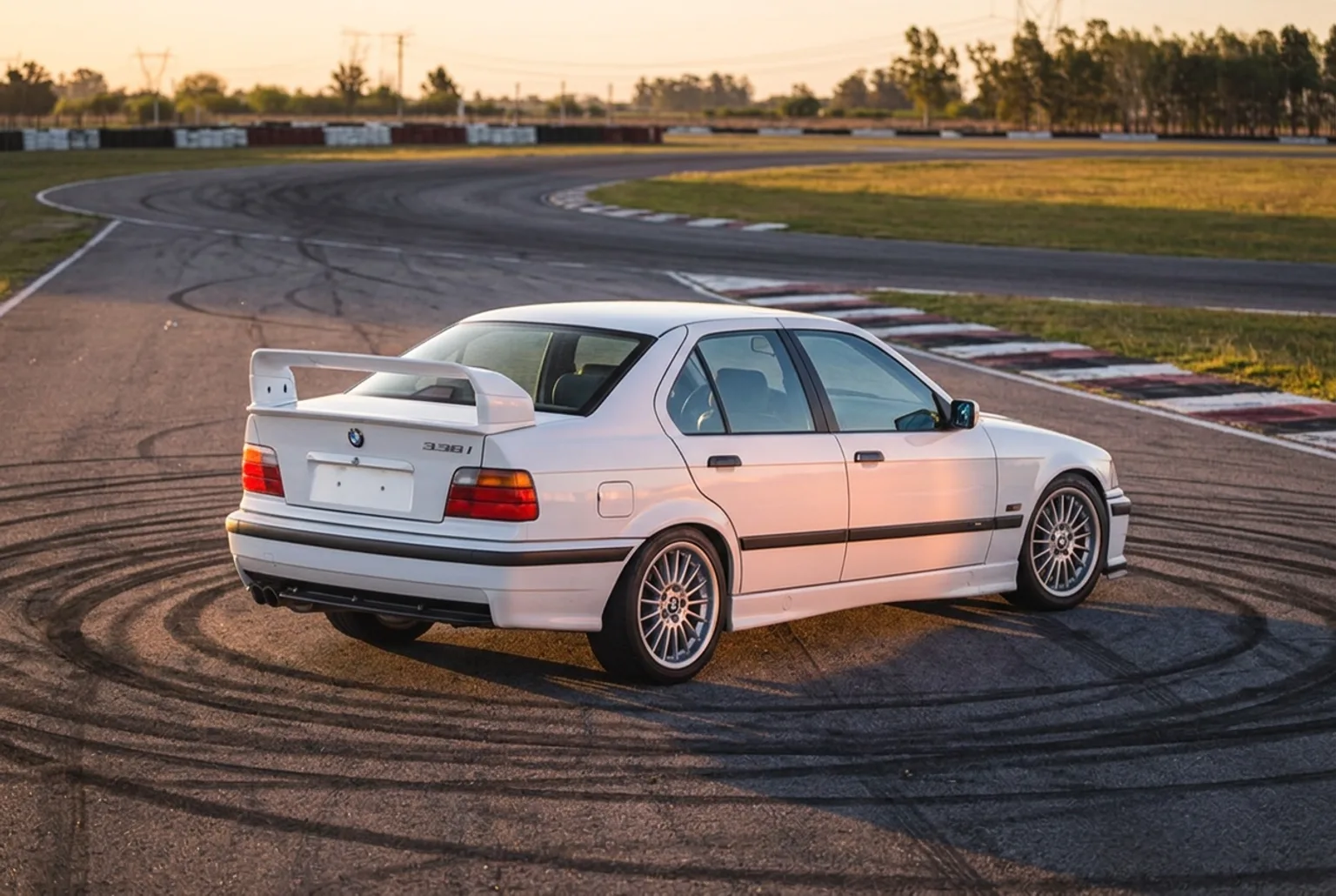 BMW E36 blanco estacionado en la hora dorada rodeado de circulos negros de goma quemada en el asfalto del autodromo