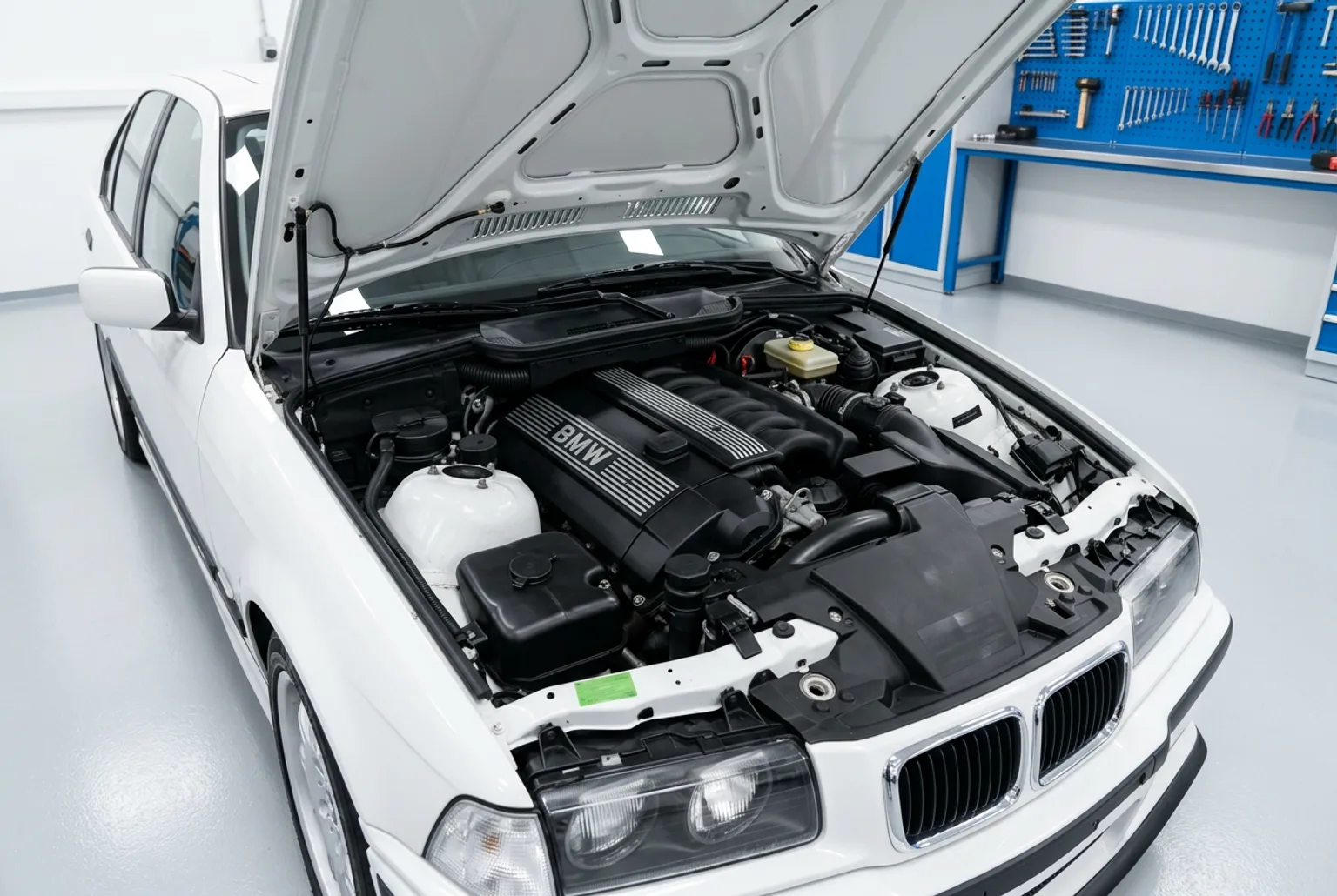 Vano motor abierto del BMW E36 blanco con el seis en linea M52 completo y limpio, en un taller impecable de piso gris claro