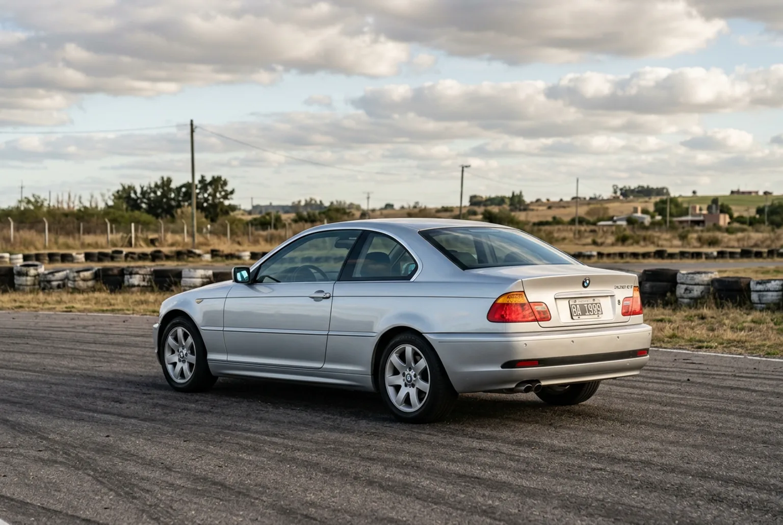 BMW E46 coupe plateado de calle estacionado solo en el paddock con luz suave de tarde entre nubes