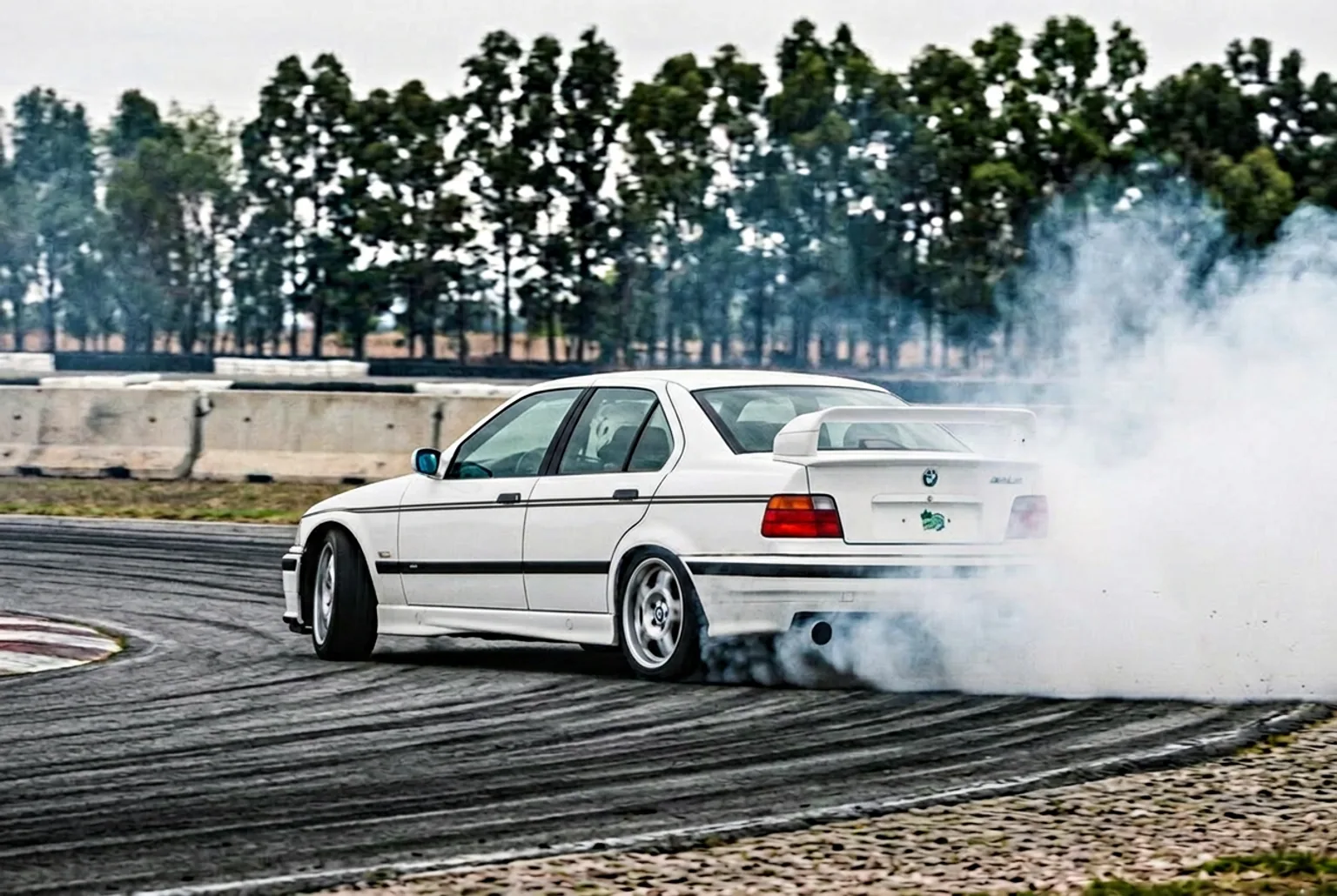BMW E36 blanco preparado para drift derrapando con humo en un autodromo cerrado de Buenos Aires