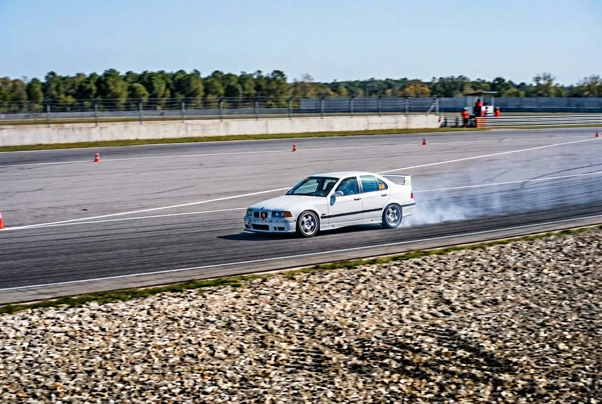BMW E36 preparado derrapando dentro das margens amplas de uma pista fechada com zona de escape de brita