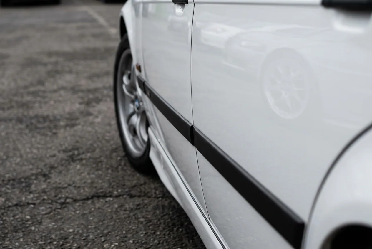 Reflejo del paddock en la pintura pulida del BMW E36 blanco, detalle de objeto de coleccion para amante de los autos en Buenos Aires