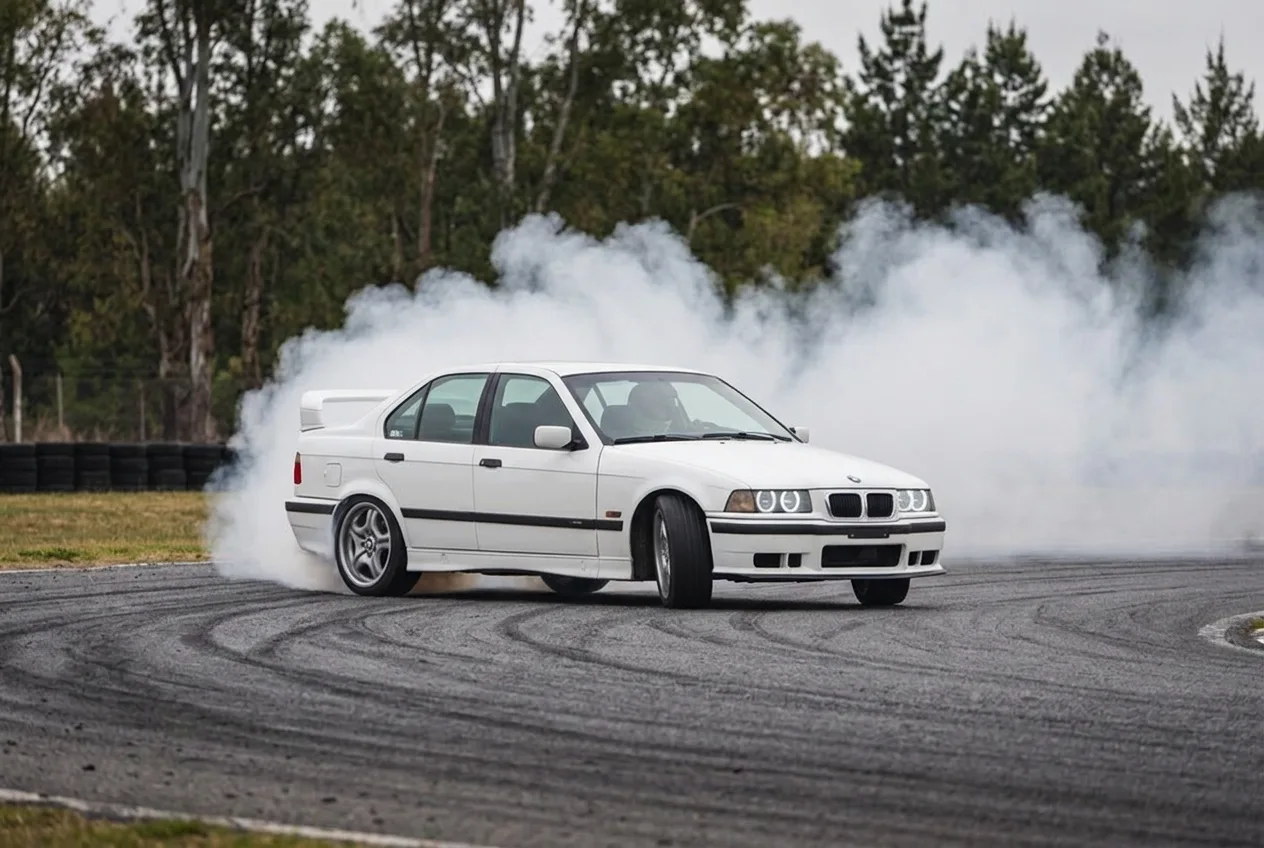 BMW E36 blanco derrapando con cortina de humo en pista cerrada de Buenos Aires, plano abierto para contenido de redes