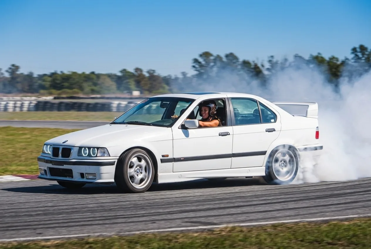 Mujer al volante de un BMW E36 blanco en pleno drift con humo, vista desde afuera por la ventanilla, en una pista cerrada de Buenos Aires