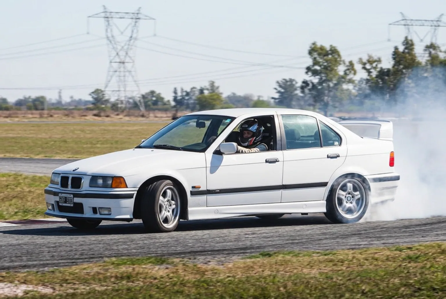 Mujer al volante de un BMW E36 haciendo drift en pista cerrada de Buenos Aires, con humo de gomas