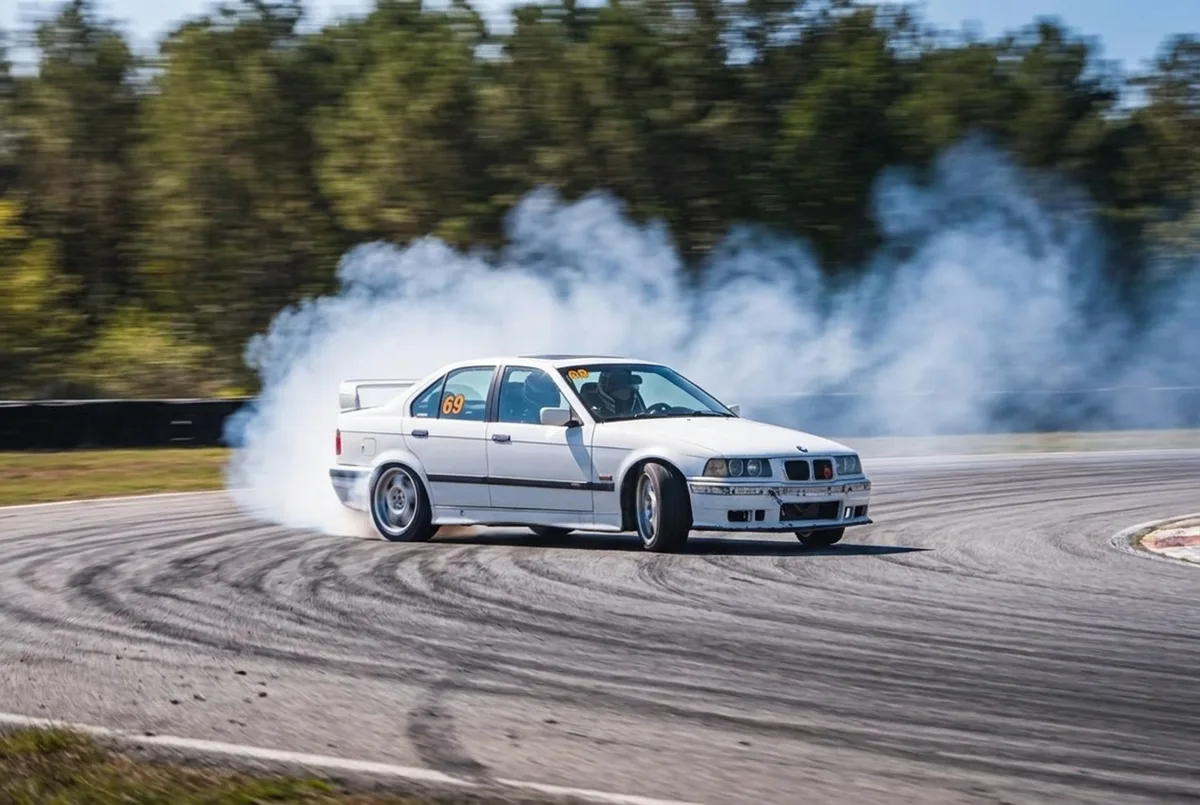 Instrutor de drift dando orientacoes a um aluno iniciante ao lado do BMW E36 na pista fechada