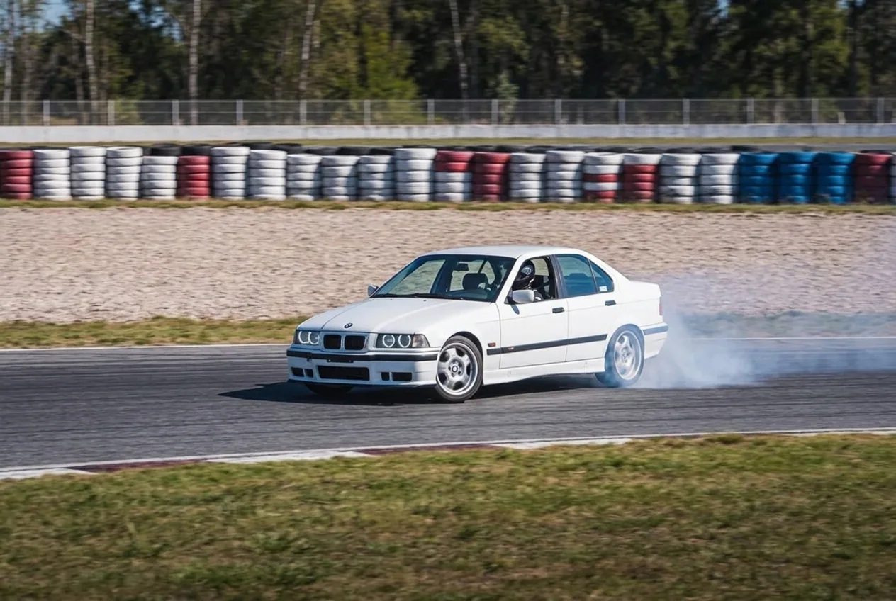 BMW E36 blanco derrapando junto a amplias zonas de escape de gravilla: el margen de seguridad de la pista