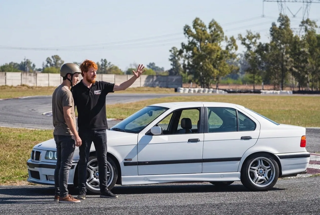 Instructor pelirrojo dando el briefing junto al BMW E36 blanco, explicando el sobreviraje antes de subir
