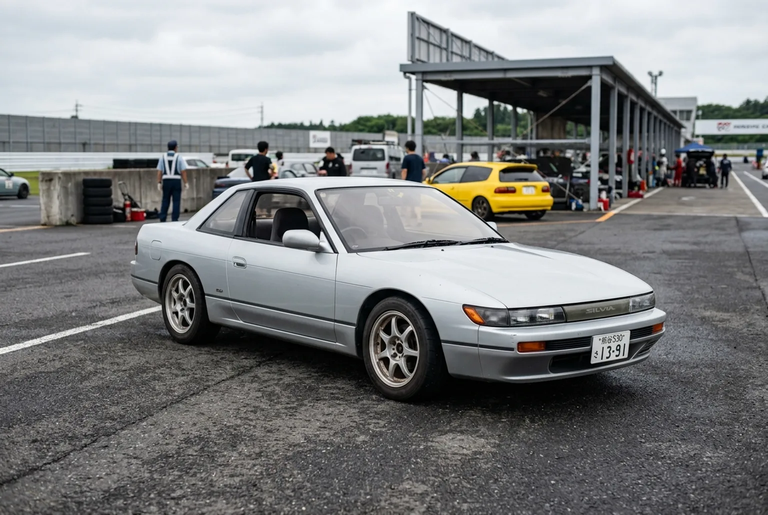 Nissan Silvia S13 plateada, cupé japonés clásico de drift, estacionada en el paddock de un autódromo