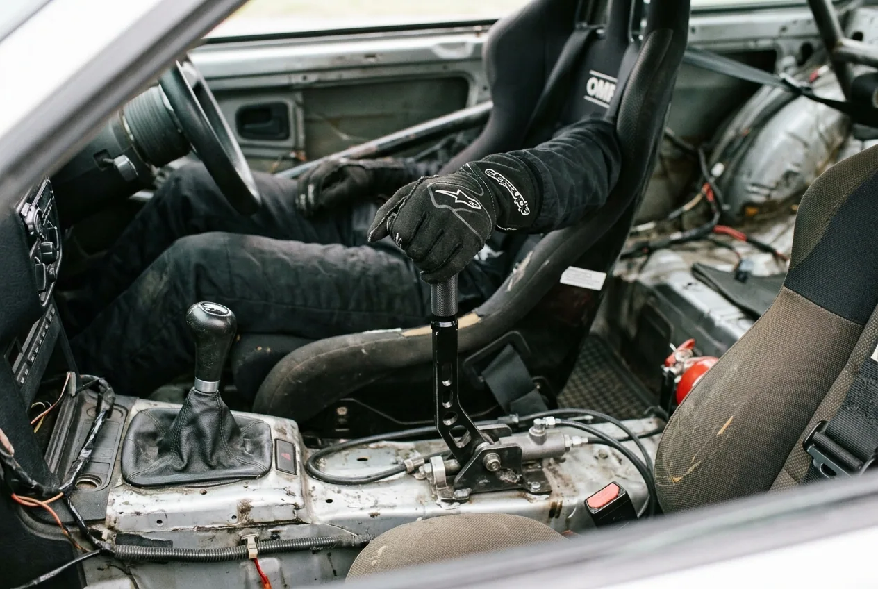 Mano enguantada tirando del freno de mano hidraulico del BMW E36: el handbrake, una tecnica que sigue al contravolante
