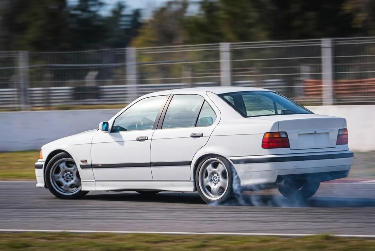 BMW E36 blanco en el instante en que el tren trasero rompe y arranca el derrape, con el primer humo