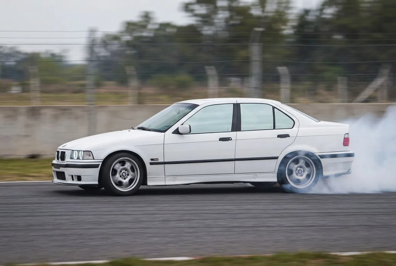 BMW E36 blanco manteniendo el derrape en angulo estable con contravolante constante y una larga estela de humo
