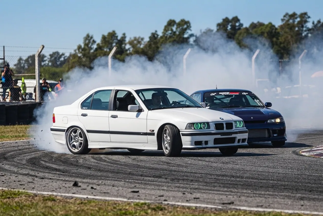 Dos autos en tandem: el BMW E36 blanco liderando y otro auto persiguiendo de cerca con humo