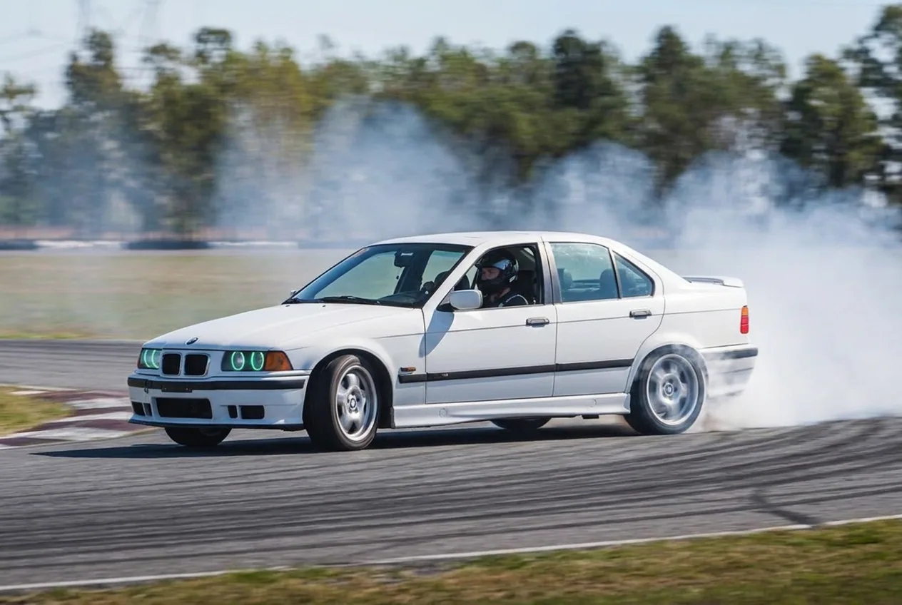 BMW E36 blanco derrapando en pista de asfalto, la superficie estandar donde se aprende drift
