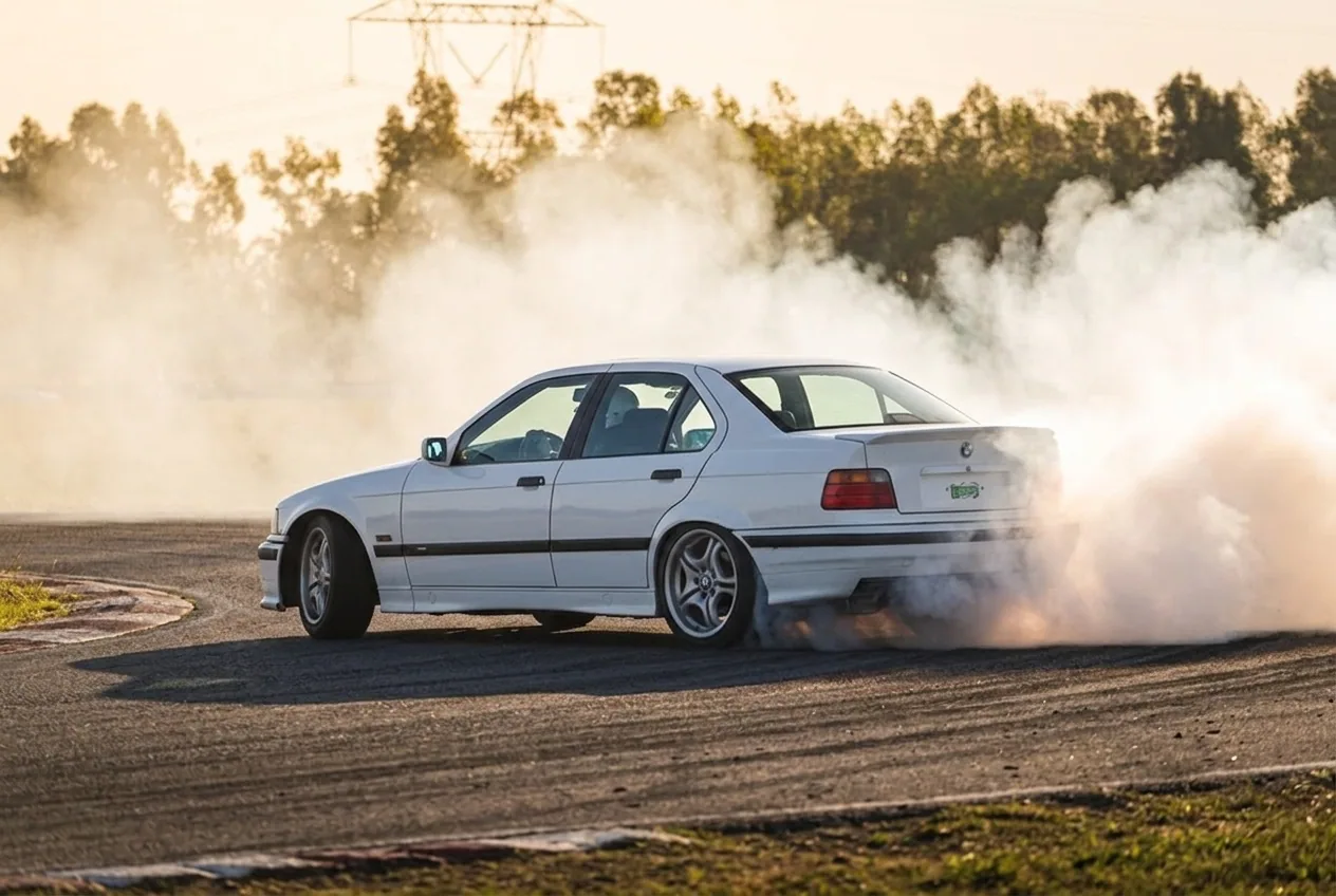 BMW E36 blanco drifteando con humo al atardecer en una pista cerrada de Buenos Aires